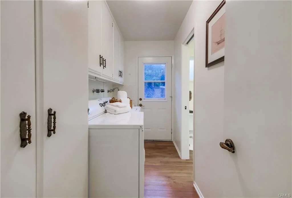 Laundry room with white cabinets, washer and dryer, wooden floor, and door to outside.