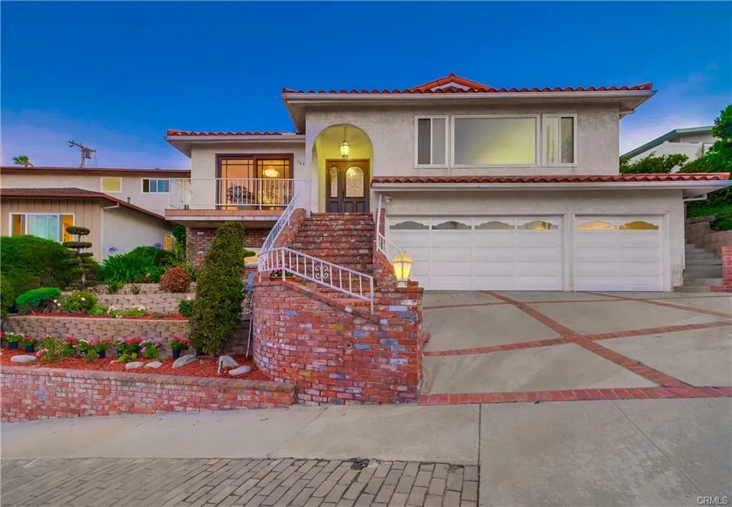 Two-story house in California real estate with red tile roof, driveway, garage, steps, windows, and greenery
