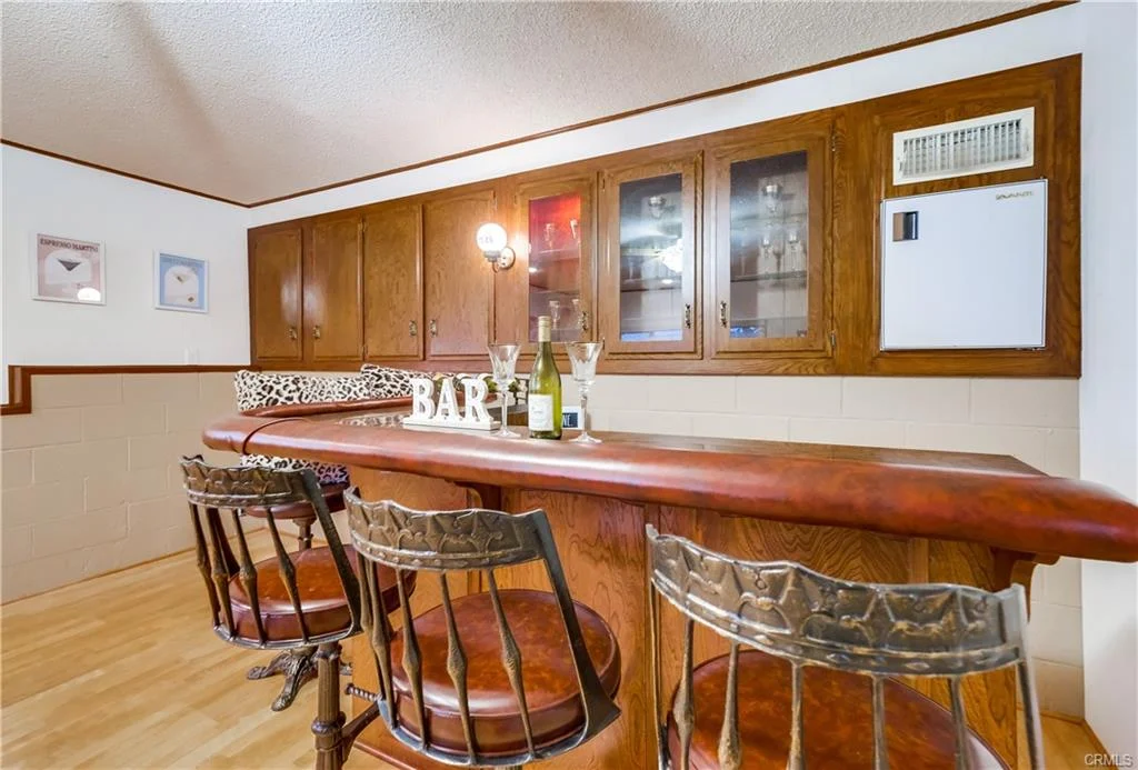 Living room with ceiling fan, sectional sofa, large windows, wooden accents, and counter with wine bottles.