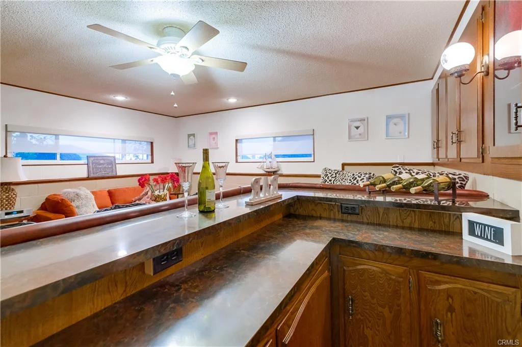 Living room with ceiling fan, sectional sofa, large windows, wooden accents, and counter with wine bottles