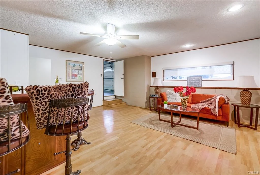 Living room with wood floor, sofa, coffee table, ceiling fan, bar stools, flowers, and wall art