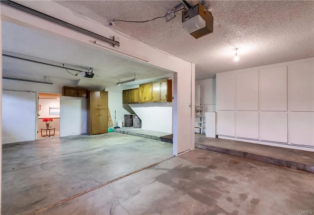 Garage with concrete floor, white walls, cabinets, two bays, and door
