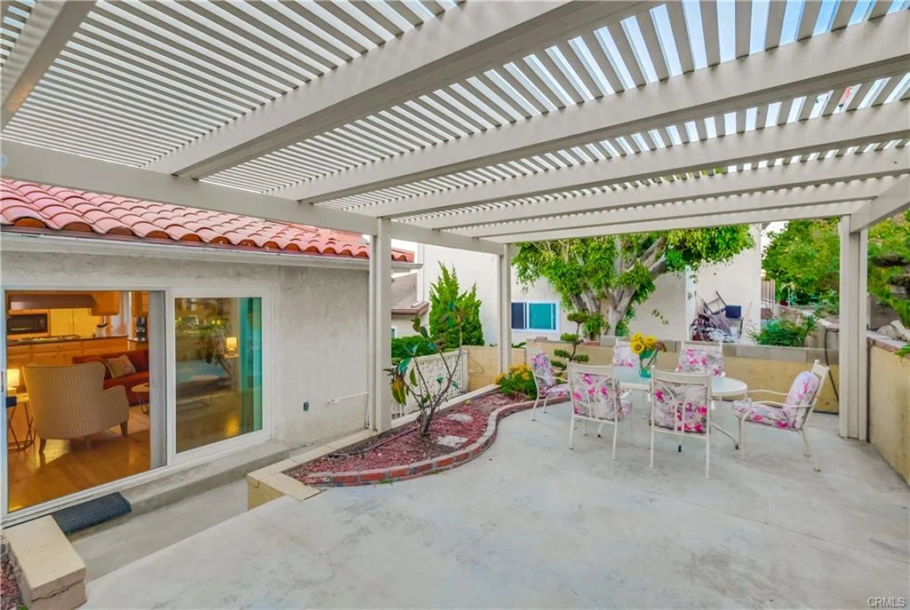 Patio with table, chairs, pergola, greenery, and sliding door outside house in California real estate
