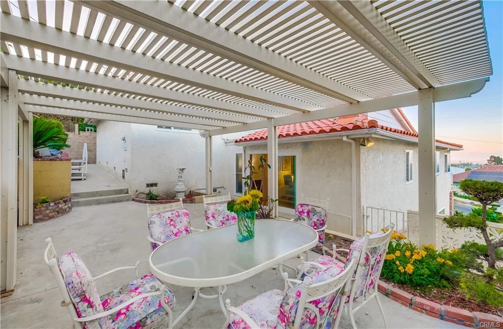 Patio with table, chairs, pergola, plants, flowers, and wall water feature outside house in California real estate