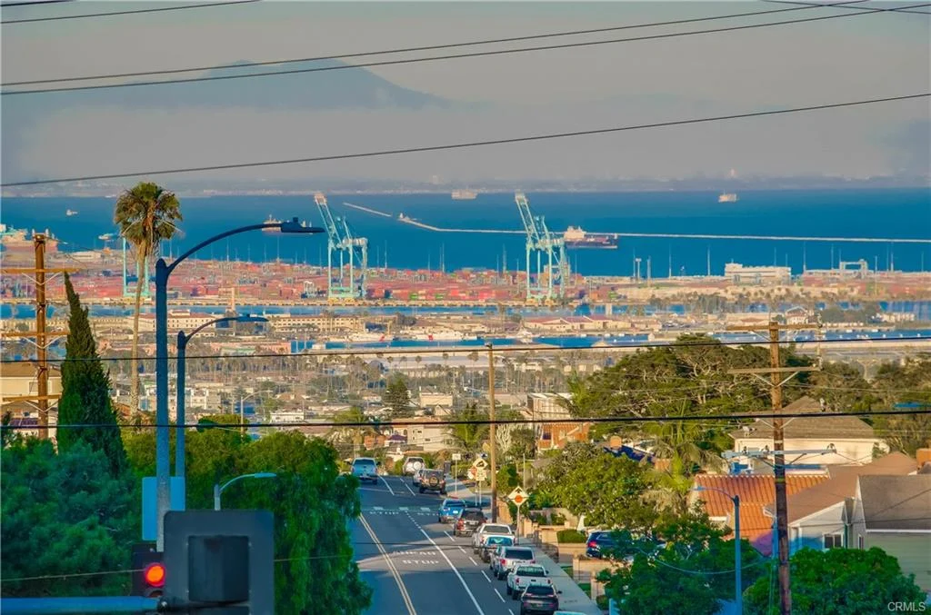 Harbor view with cranes, ships, palm trees, street, and houses in California real estate