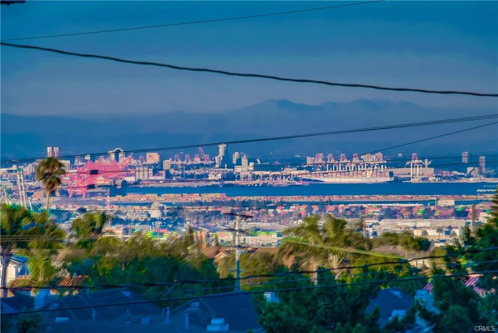 Coastal cityscape with harbor, shipping containers, cranes, hills, and palm trees