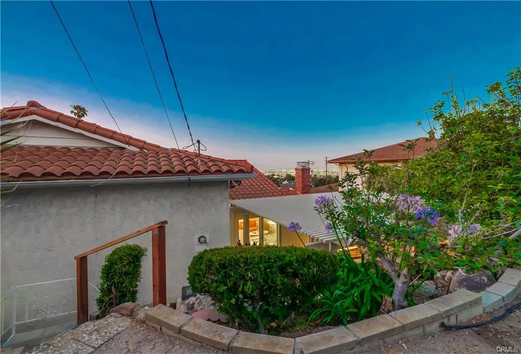 Hillside house in California real estate with terracotta roof, pathway, plants, and flowers