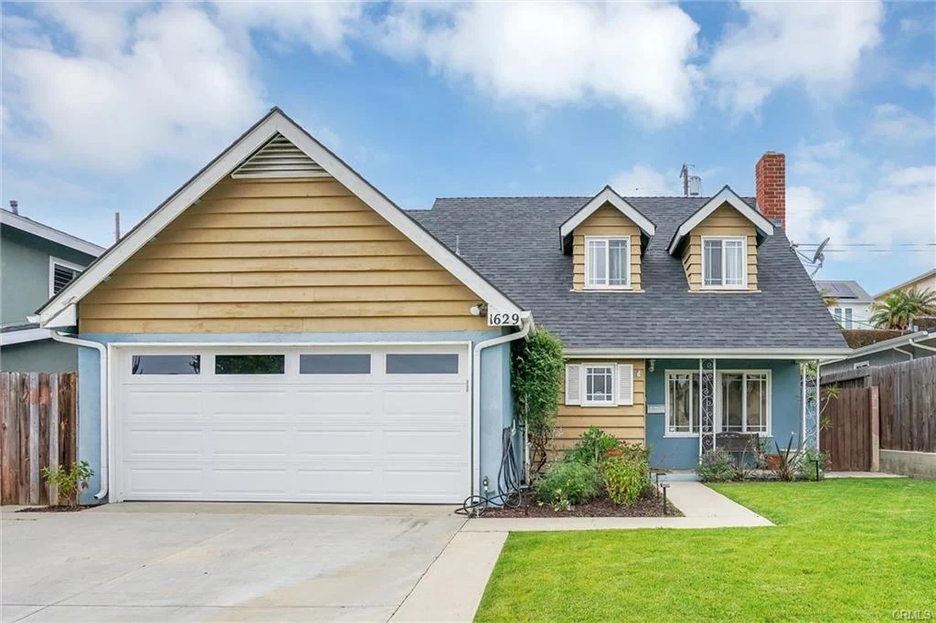 California real estate house with blue and beige siding, sloped roof, garage, porch with plants, and driveway.