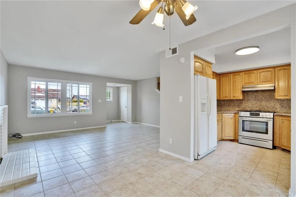 Kitchen and living area with tile floor, beige walls, wooden cabinets, and ceiling fan.