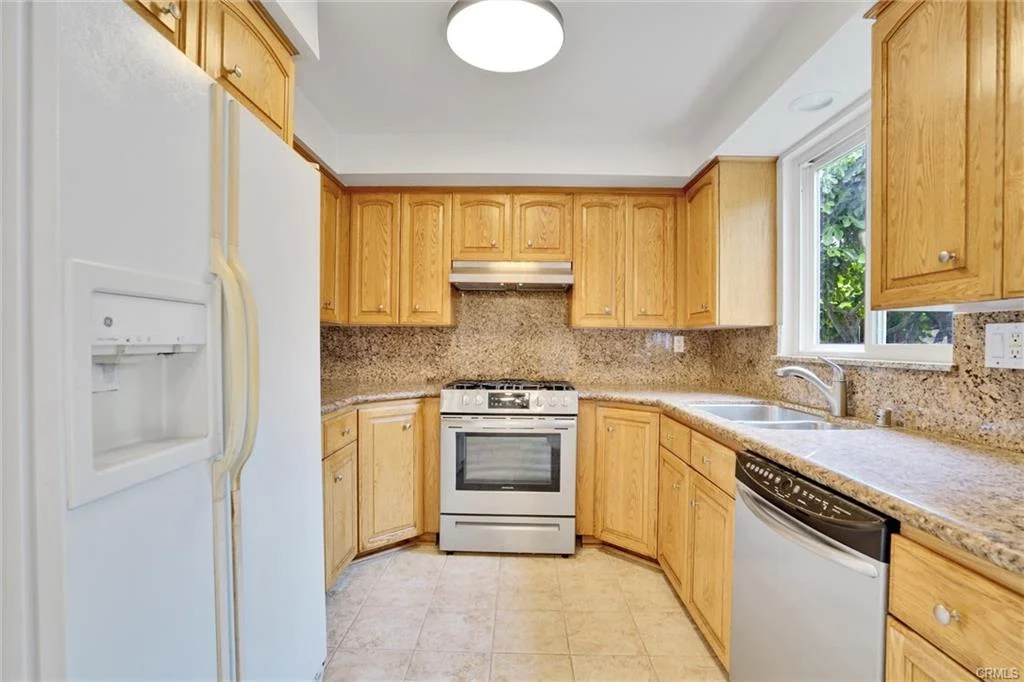 Kitchen with wooden cabinets, stainless steel stove and dishwasher, granite countertops, and window above sink.