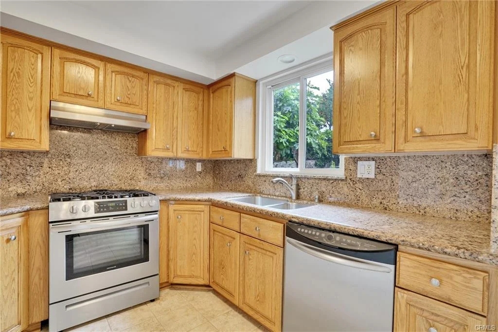 Kitchen with wooden cabinets, granite countertops, stainless steel stove and dishwasher, and window.