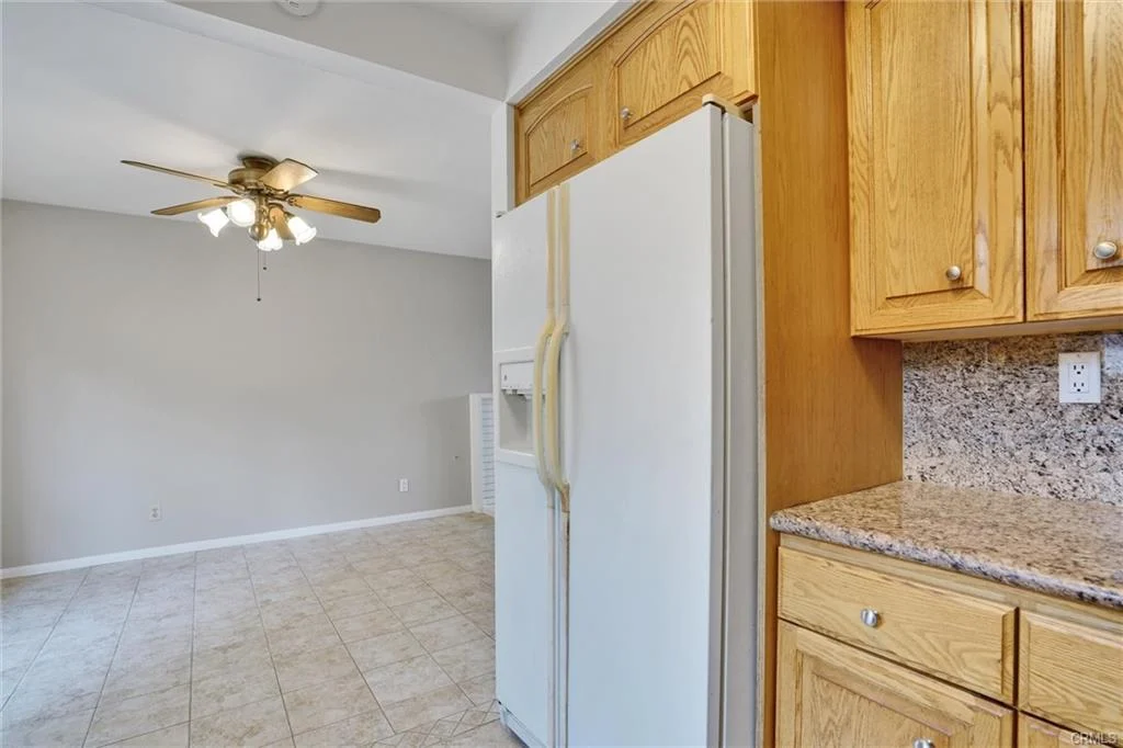 Kitchen with wooden cabinets, refrigerator, granite countertops, and ceiling fan in living area.