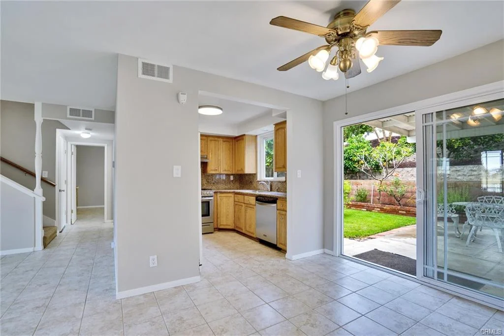 Kitchen and dining area with tile floor, wooden cabinets, stainless steel appliances, ceiling fan, and sliding glass door to patio.
