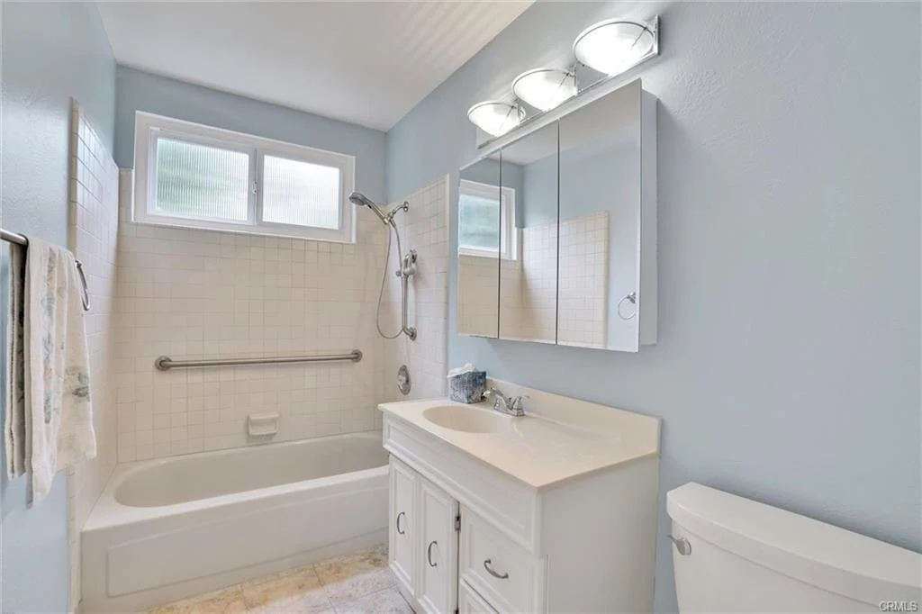 Bathroom with light blue walls, bathtub with shower, white vanity, toilet, and mirrors.