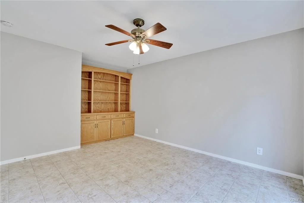 Room with light walls, tiled floor, ceiling fan, and wooden bookshelf.