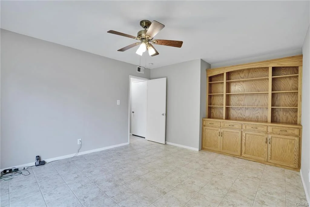 Room with light walls, ceiling fan, wooden shelves, tiled floor, and open door.
