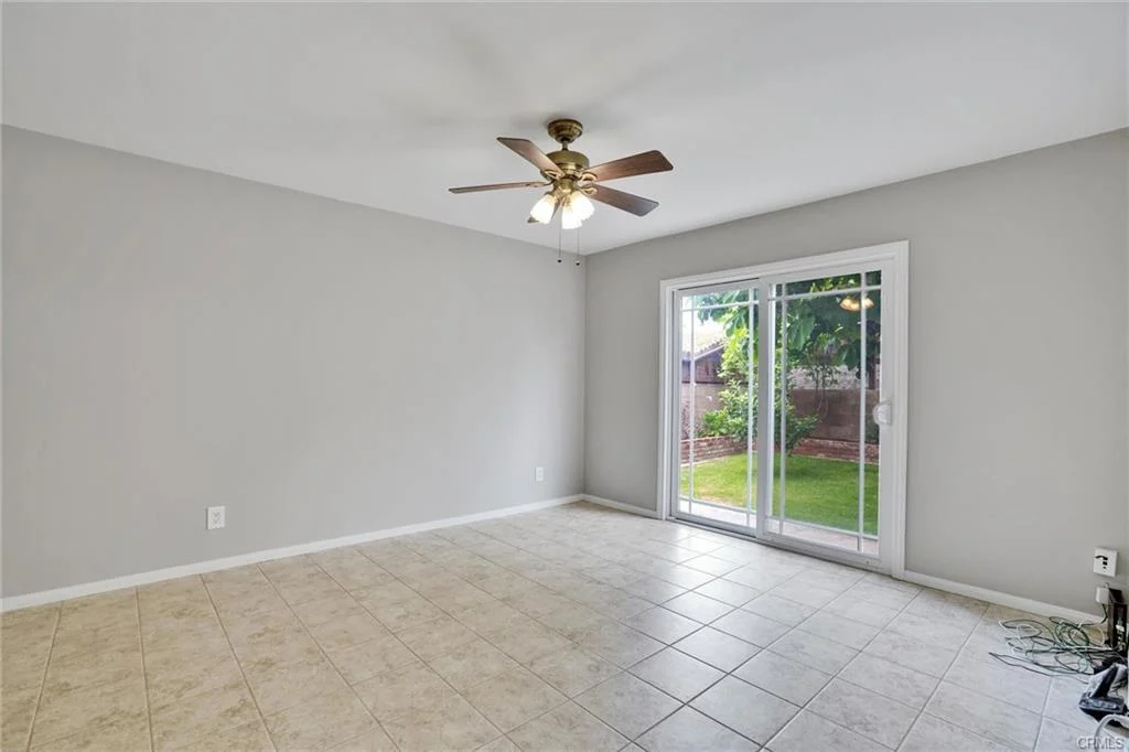 Room with light gray walls, tile floor, ceiling fan, and sliding glass doors to yard.