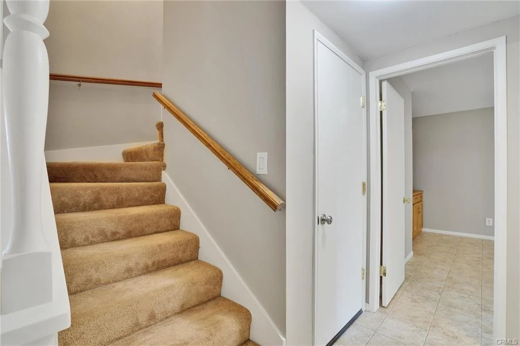 Carpeted staircase leading up with hallway and door to room with tile floor.
