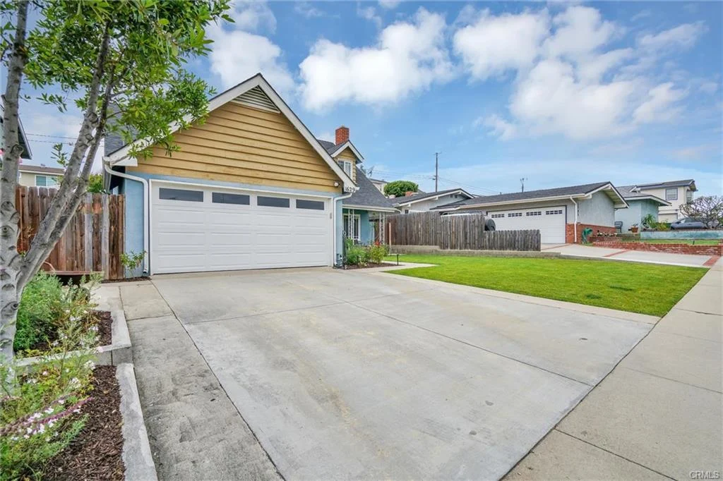California real estate house with blue and beige siding, sloped roof, garage, porch with plants, and driveway.