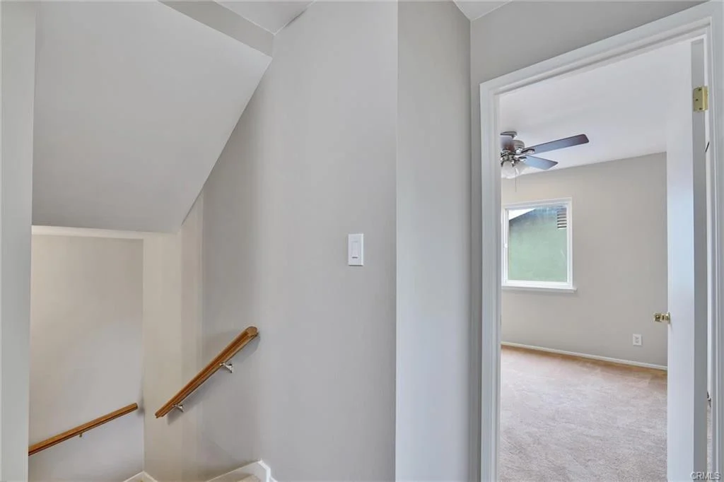 Staircase leading up with hallway and open door to room with light walls and carpet.