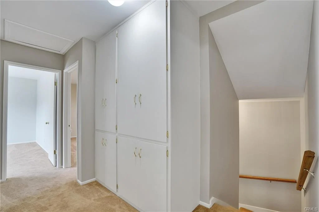Hallway with beige carpet, white walls, built-in closets, and staircase.