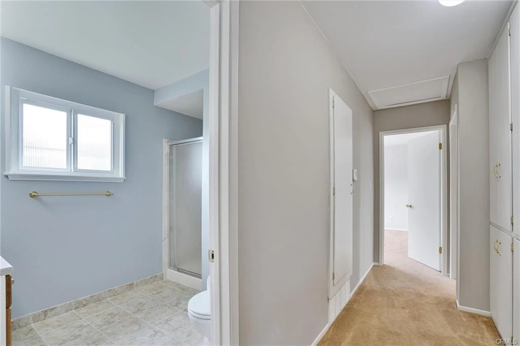 Bathroom with shower, toilet, window, and hallway with light walls and floor.