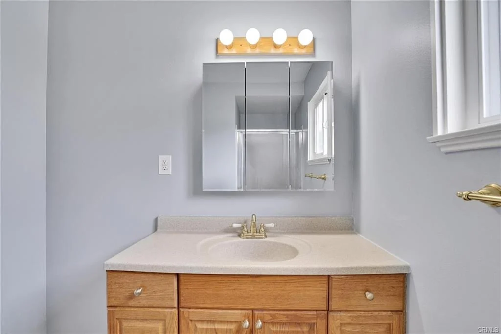 Bathroom with sink, lighted mirror, wooden cabinets, and gray walls.