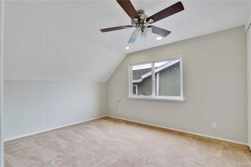 Room with beige carpet, ceiling fan, light-colored walls, and window.