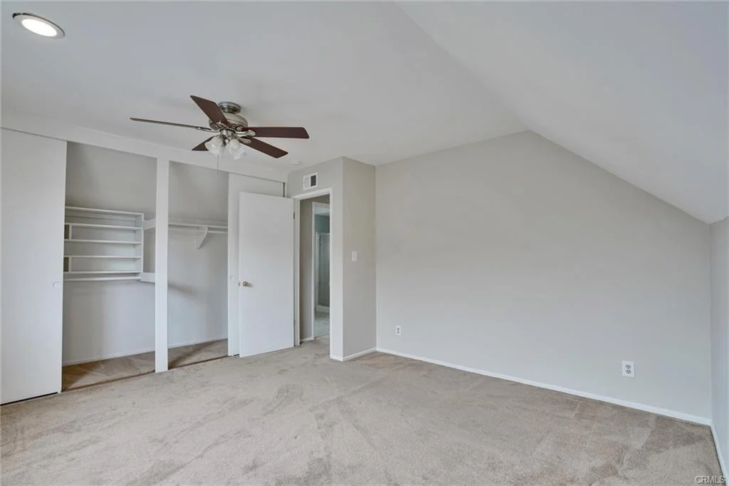Room with sloped ceiling, carpet, ceiling fan, closet, and open door.