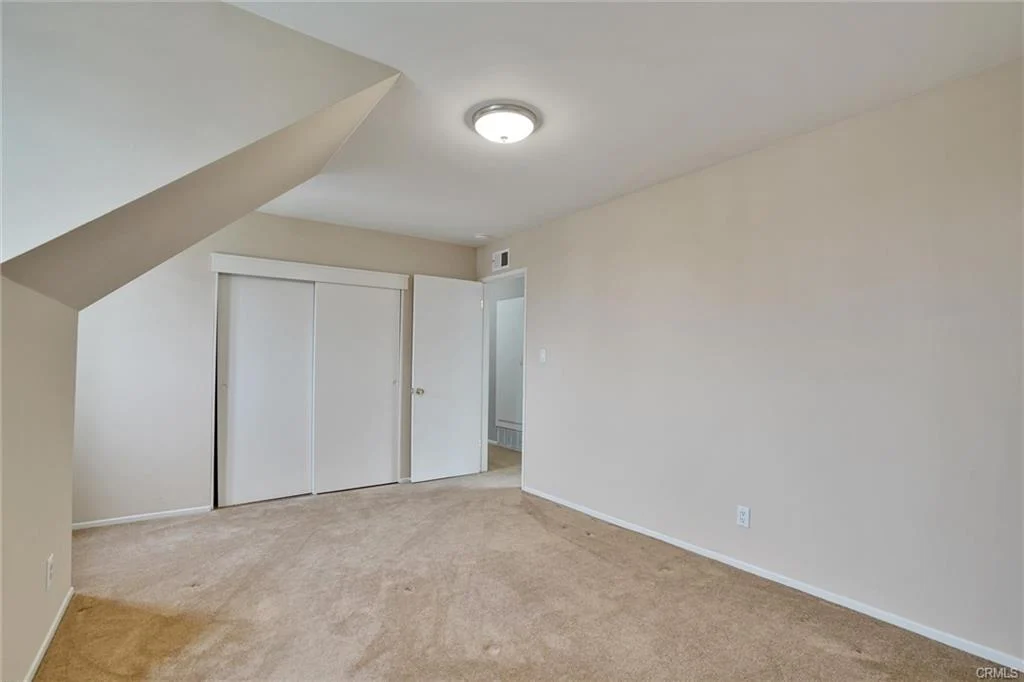 Room with beige walls and carpet, angled ceiling, light fixture, and two closet doors.