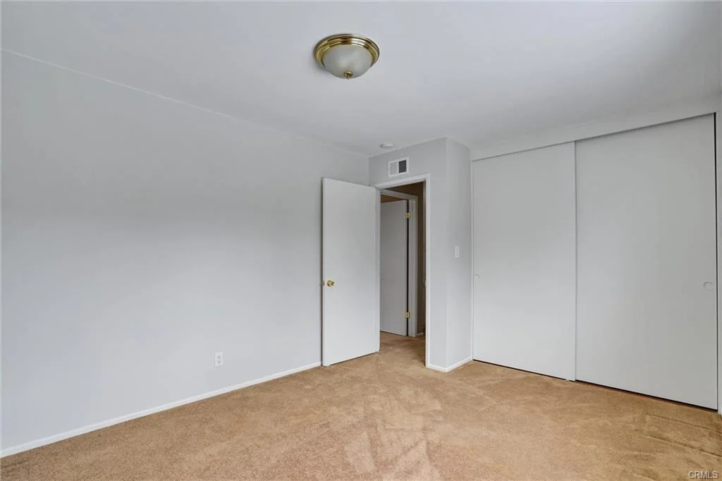 Room with beige carpet, white walls, ceiling light, open door, and sliding closet.