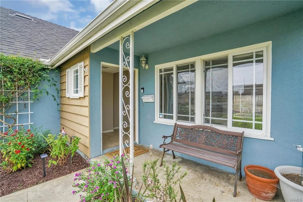 California real estate house with porch bench, plants, and white window shutters.