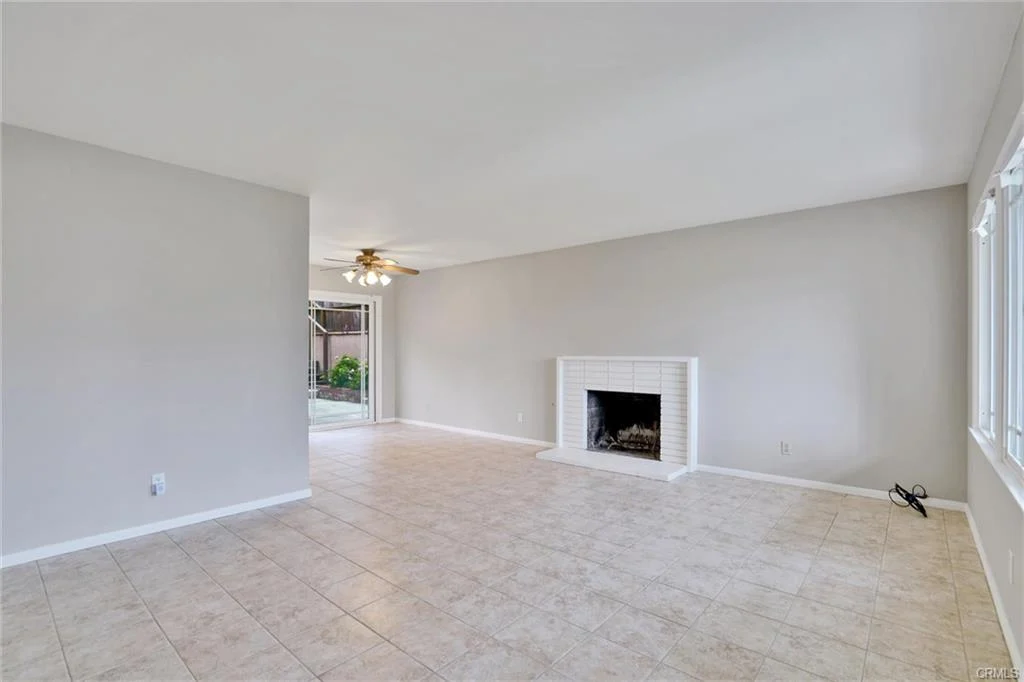 Living room with tile floor, gray walls, ceiling fan, fireplace, and large windows.