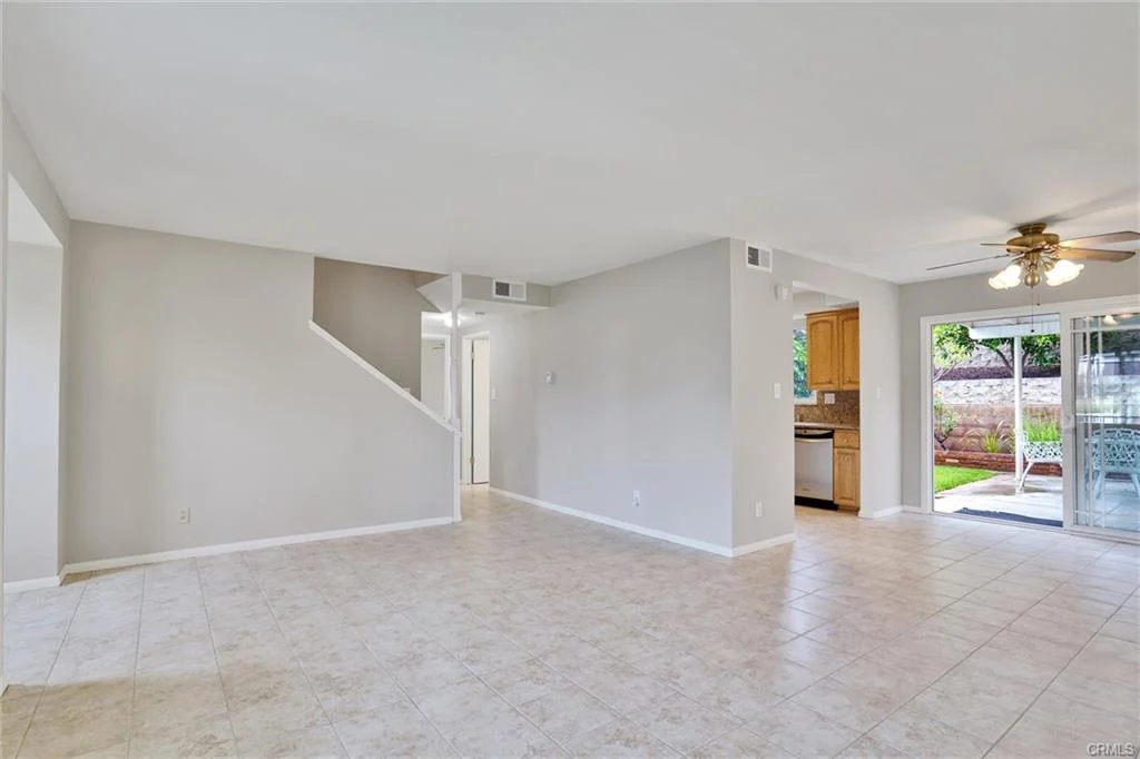 Living area with tile floor, staircase, sliding glass doors, and kitchen in background.