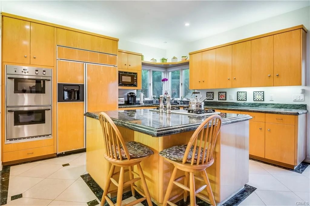 Kitchen with yellow cabinetry, black granite island, stools, and appliances.