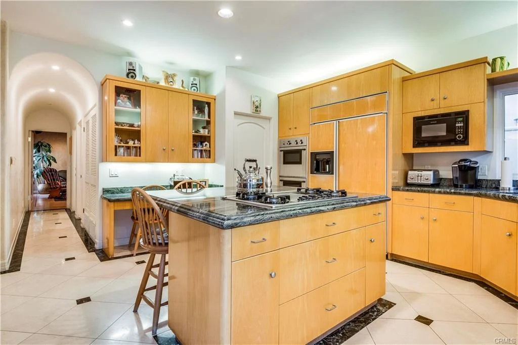 Kitchen with light wood cabinetry, large island, stove, and appliances.