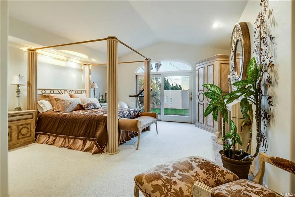 A bedroom with a large bed, plant, and decor.