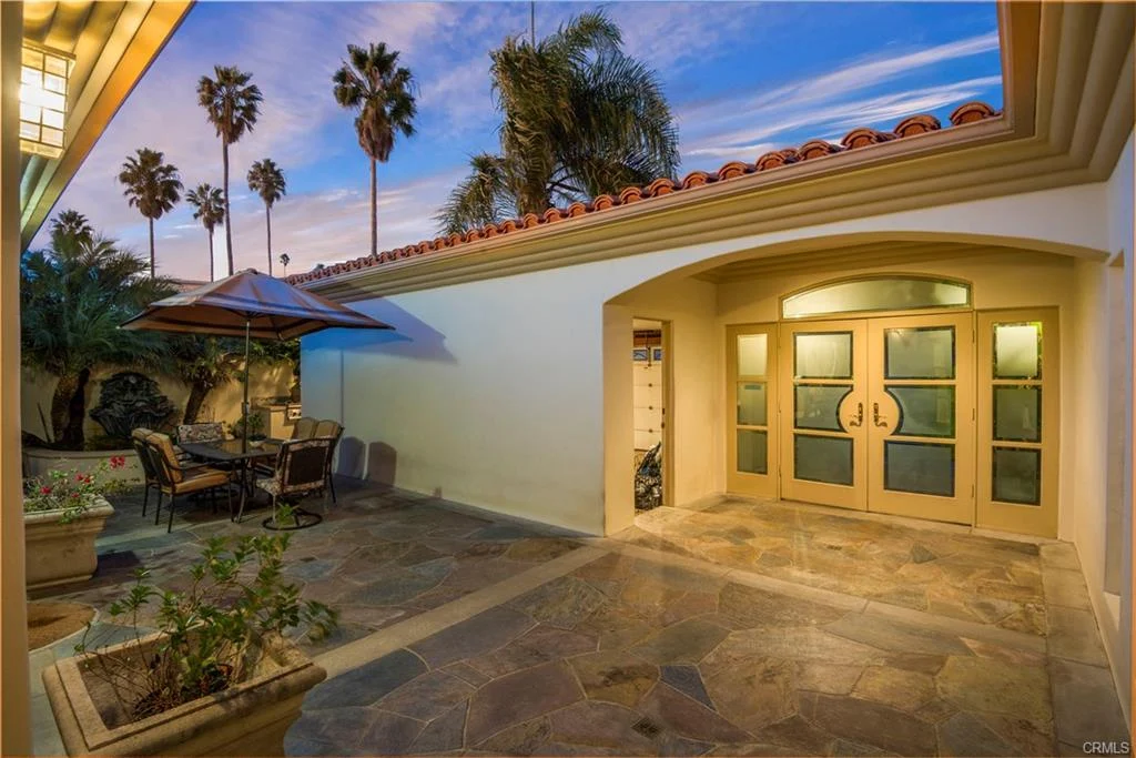 Outdoor patio with stone floor, palm trees, dining table, and house, California real estate.