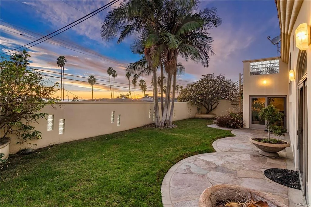A house with a green lawn, tall palm trees, and a stone path, real estate.