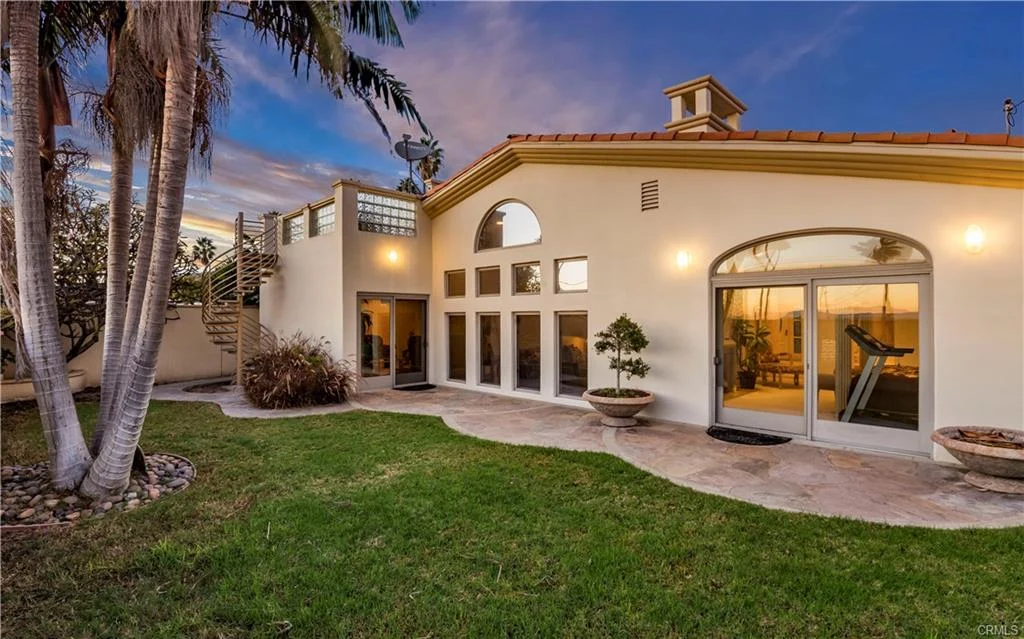 California real estate house with arched windows, green lawn, and tall palm trees.