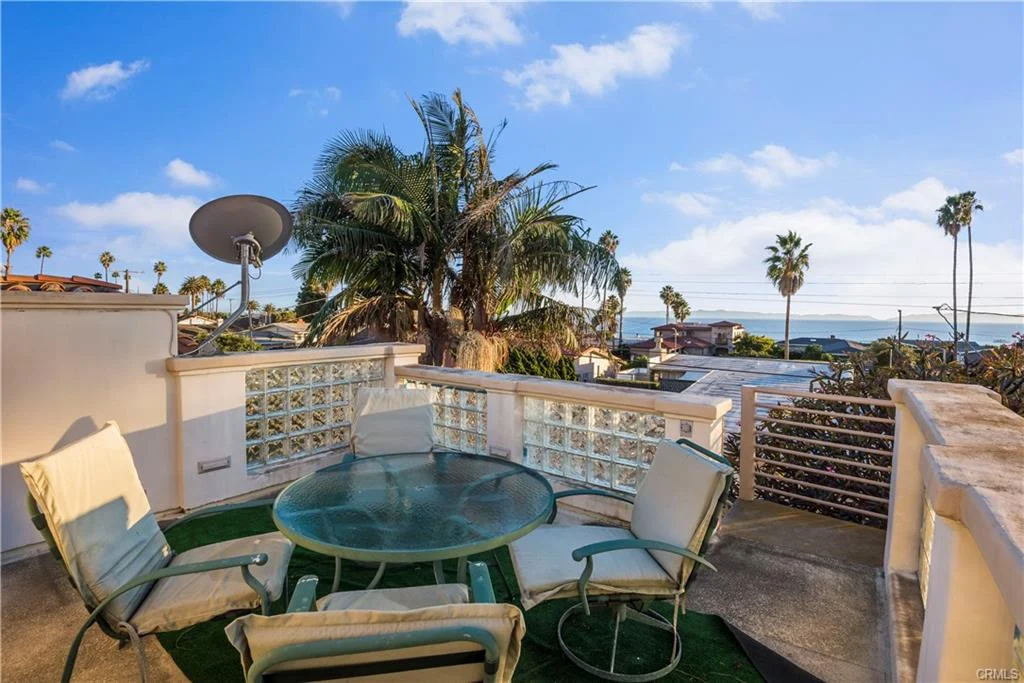 Balcony with round glass table, four chairs, palm trees, and ocean view.