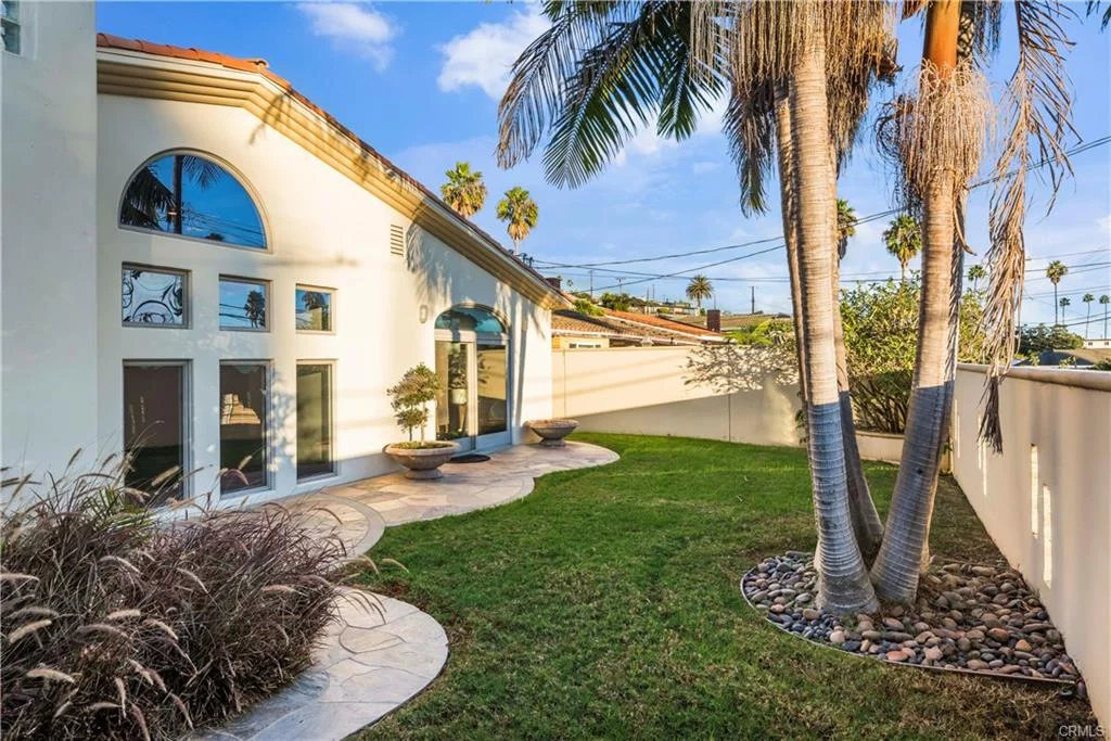 Backyard with green plants, palm trees, and stone pathway next to house.
