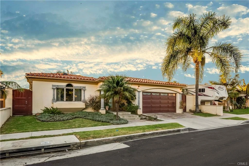 California real estate house with tile roof, front yard, driveway, and palm trees.