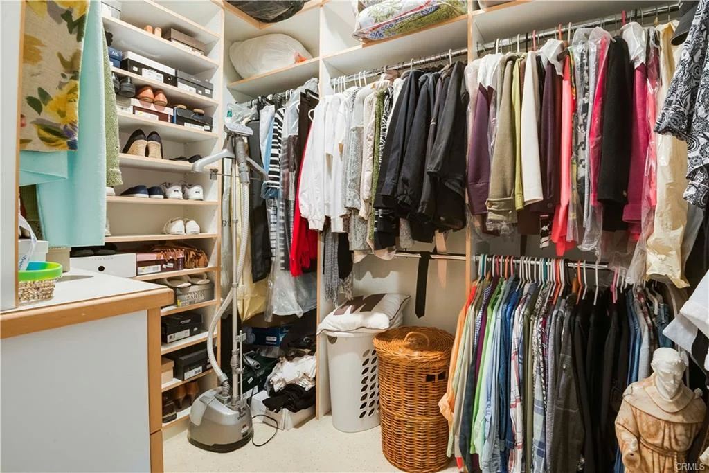 Closet with hanging clothes, shelves with shoes, laundry basket, and vacuum cleaner.