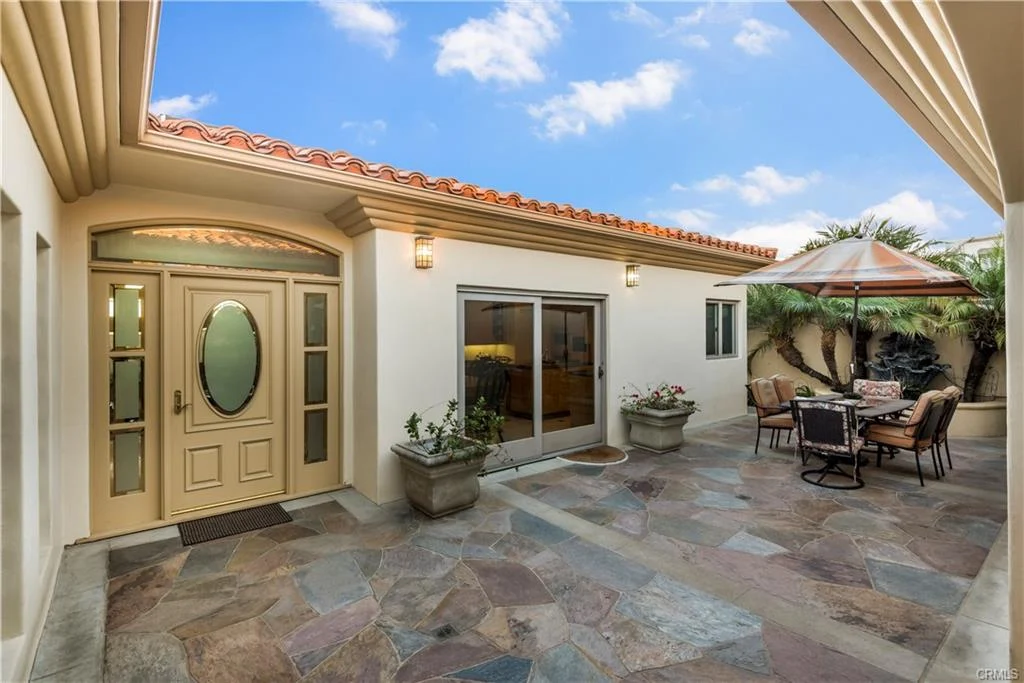 Patio with stone flooring, potted plants, dining set, and house.