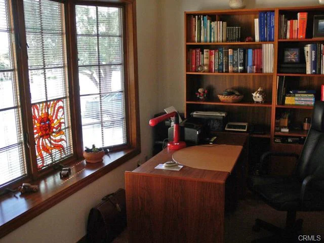 Office space with a wooden desk, a black office chair, bookshelves, and a window with a stained-glass piece.