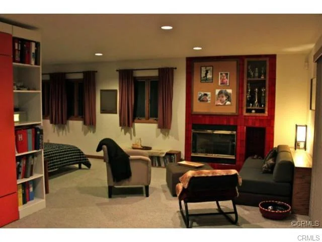 Living space with a bookshelf, sofa, armchair, a window with curtains, a fireplace, and framed photos.