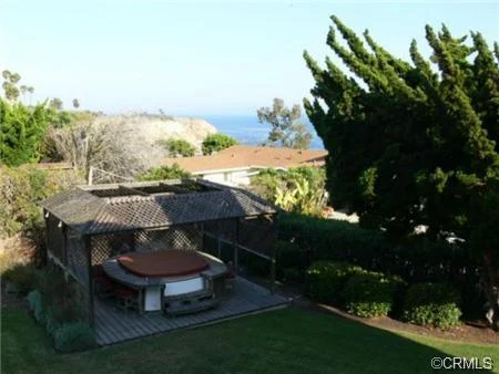Backyard with a hot tub under a pergola, greenery, and an ocean view.