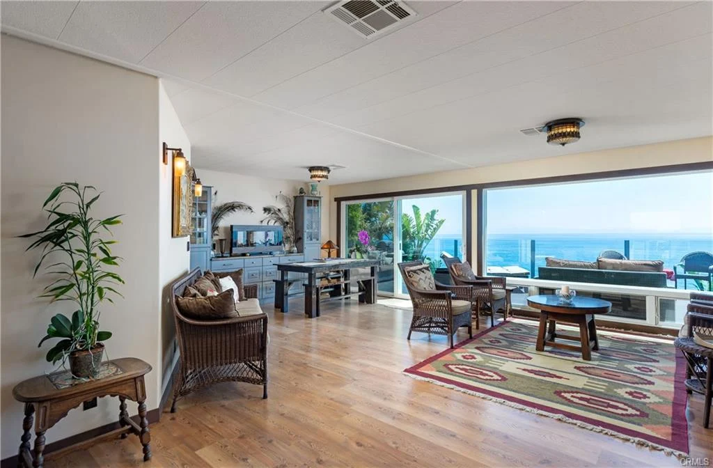 Living room with seating, coffee table, plants, wooden floor, and ocean view