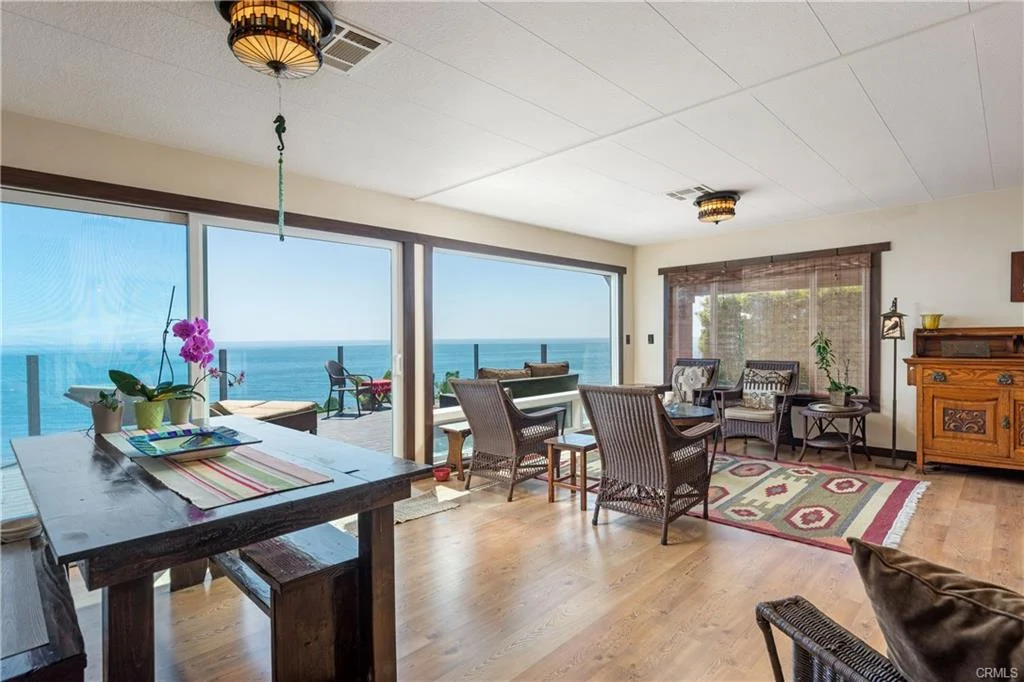 Living space with table, chairs, plants, and large windows with ocean view